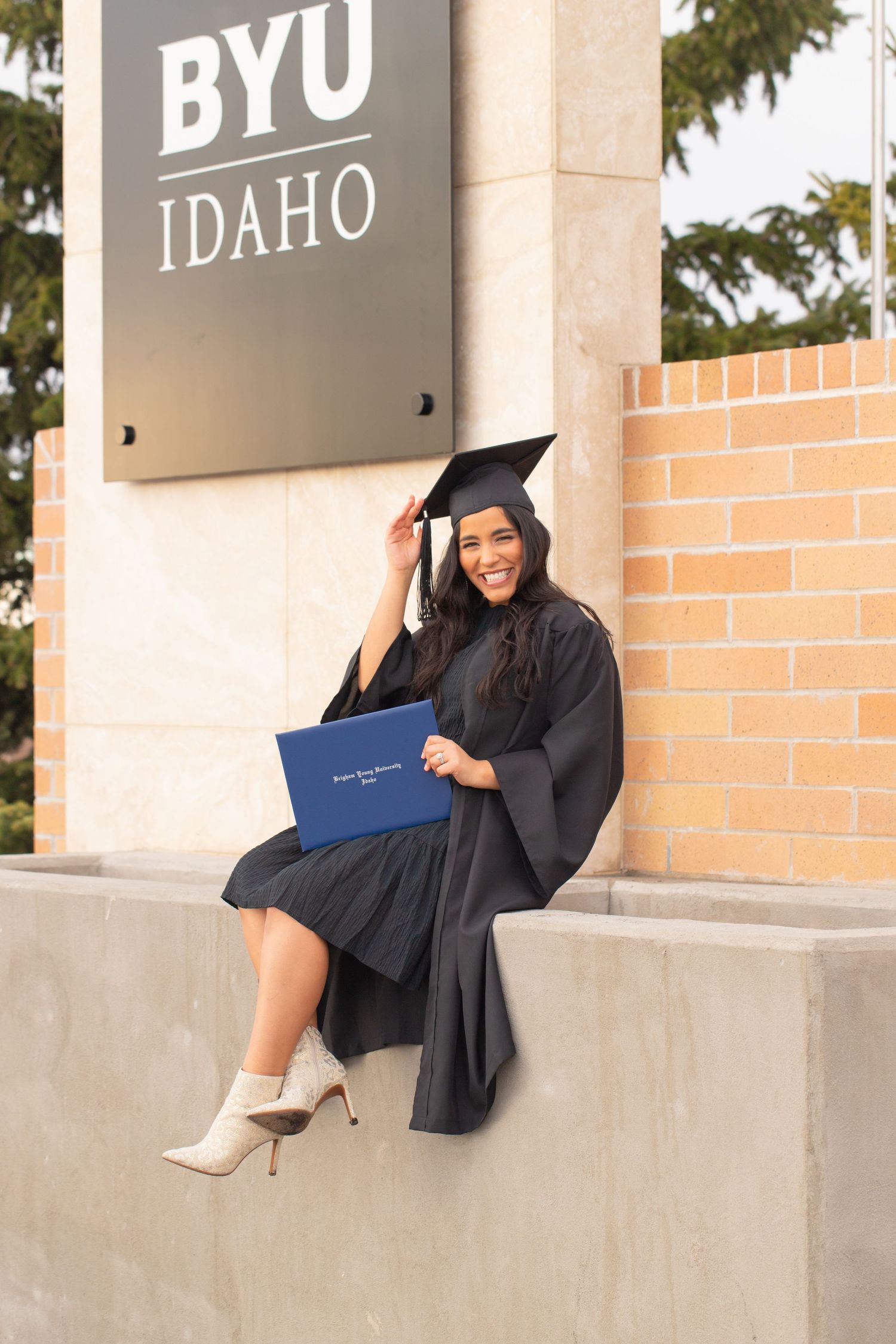 Graduate poses with diploma in front of BYU Idaho campus sign.