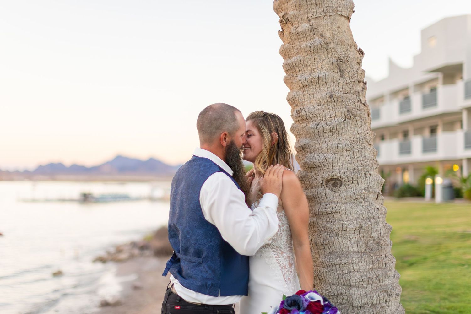 Couple embracing near palm trees during sunset with ocean view.