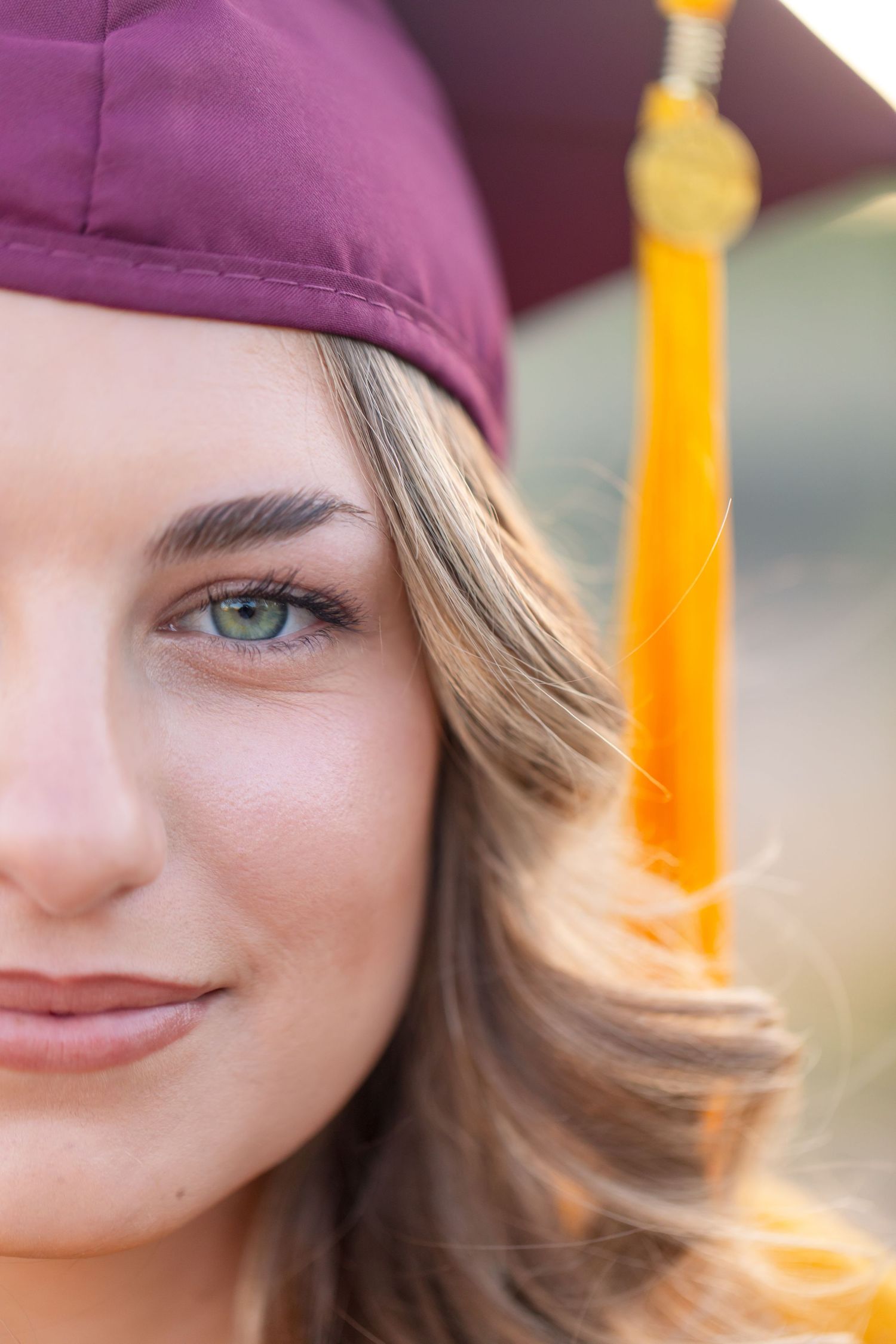 Close-up portrait of a young woman in a maroon graduation cap with gold tassel, smiling with green eyes in Lake Havasu City Arizona