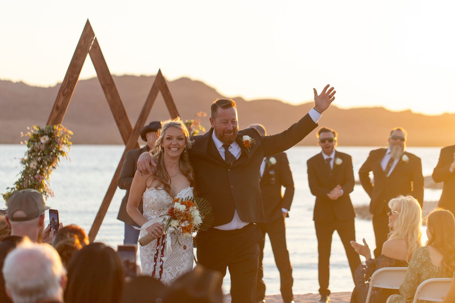 A sunset wedding ceremony on the beach with wooden triangle arches and floral decorations.
