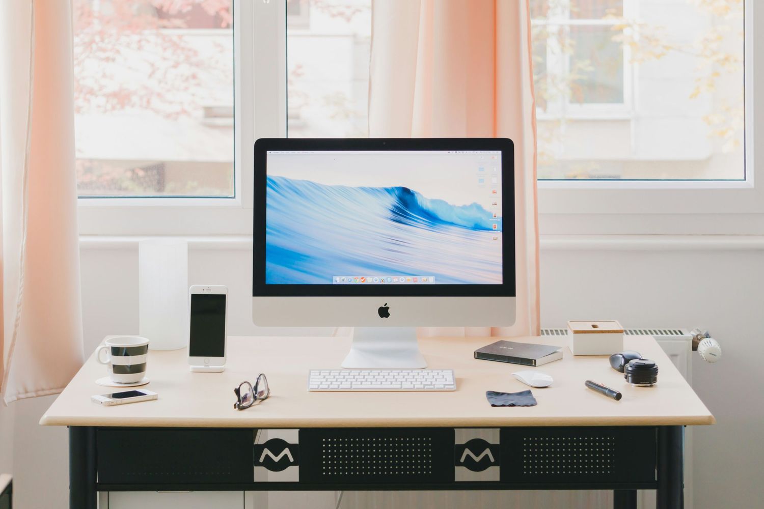 A minimalist white desk setup with an iMac computer, wireless peripherals, and modern accessories in a bright room.