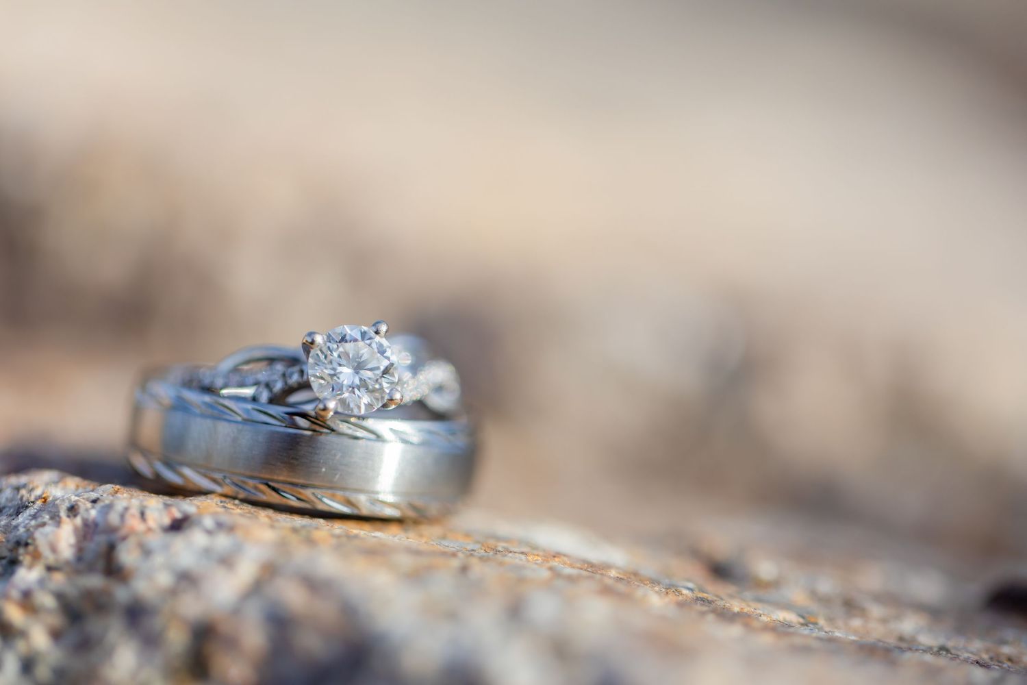 Diamond engagement ring and wedding band resting on a rocky surface with a soft bokeh background at Shugrues in Lake Havasu