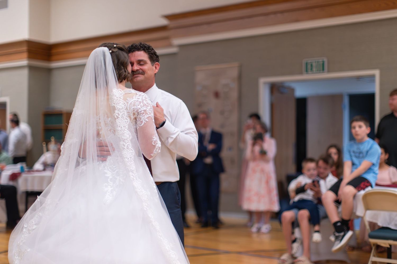 A bride and groom share their first dance together at a wedding reception in a bright banquet hall.