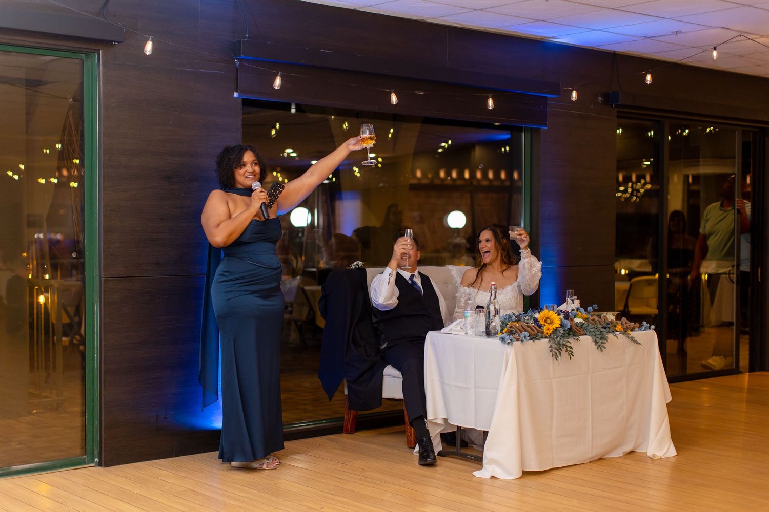 Bridesmaid gives a heartfelt toast at wedding reception while bride and groom sit at sweetheart table at Shugrues in Lake Havasu