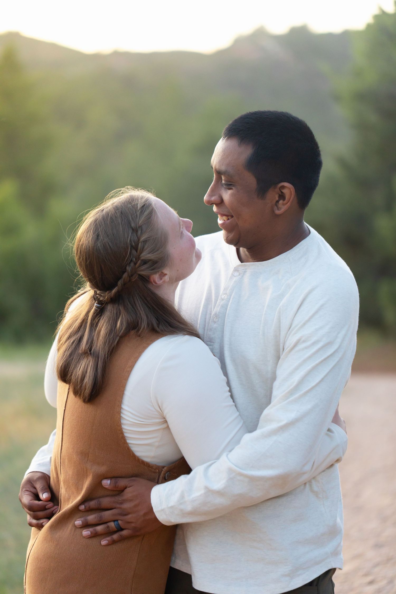 Romantic couple embracing on a beach at sunset in white clothing.