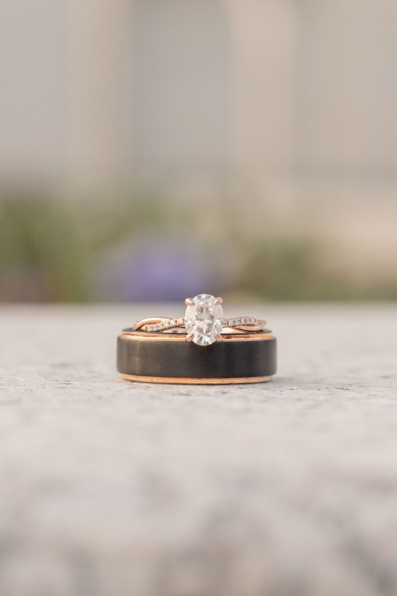 A close-up photo of a delicate rose gold engagement ring with a small diamond solitaire on a textured gray surface.