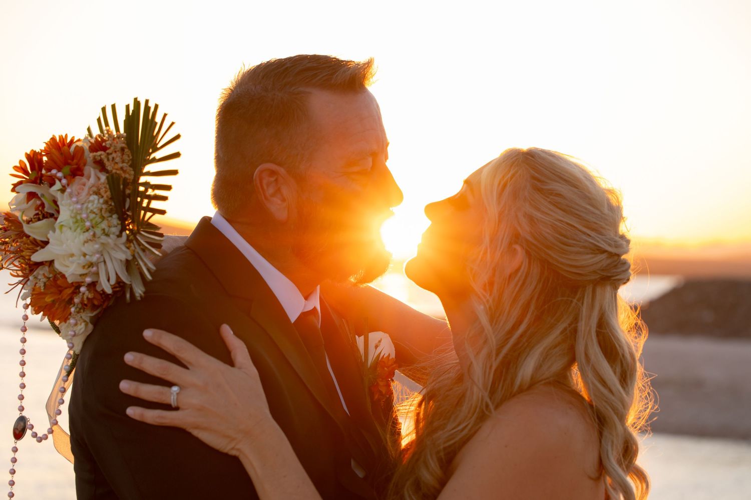 Golden sunset wedding portrait with sunburst and floral bouquet silhouette.