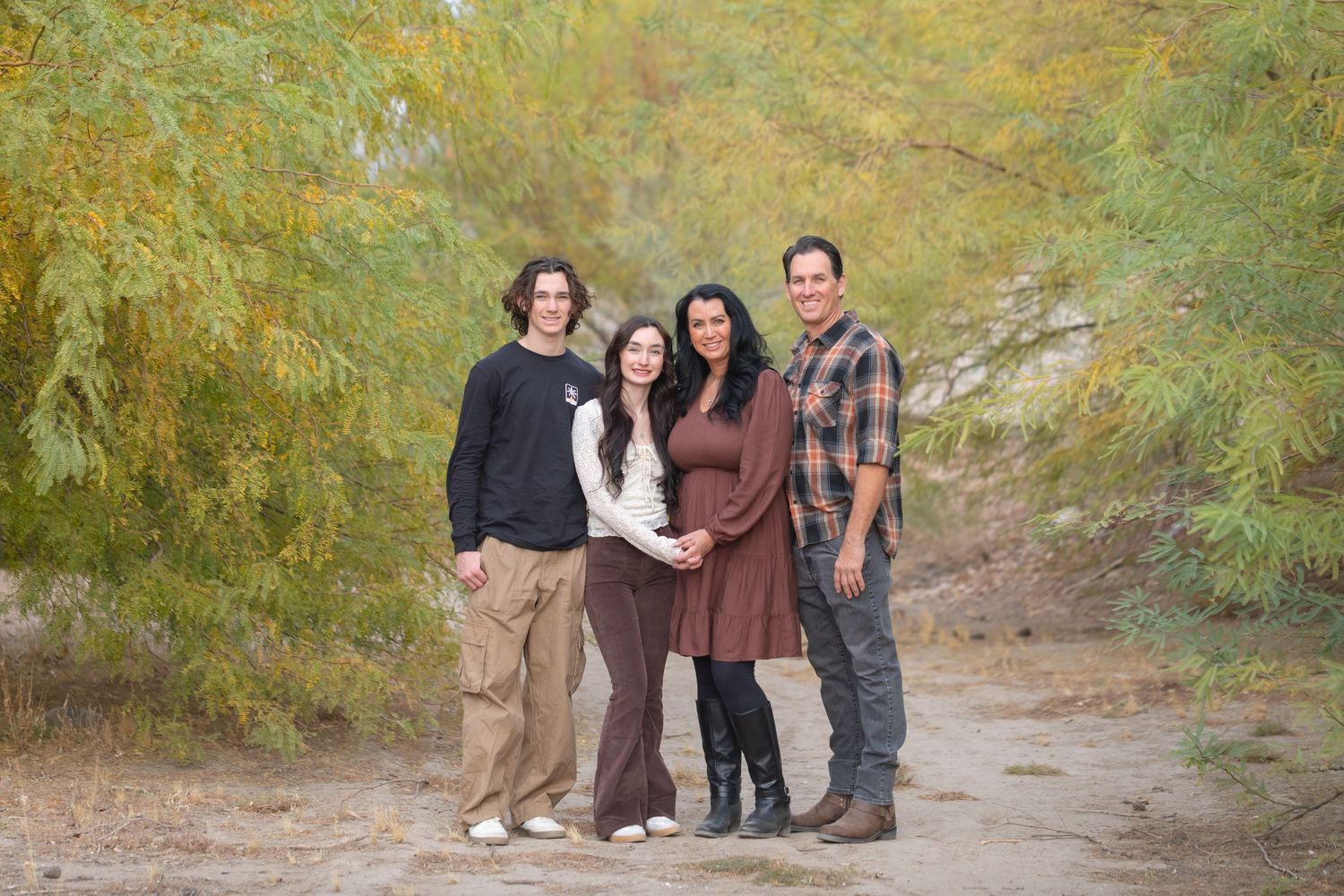 Pregnant woman poses with family of four outdoors among autumn trees on a dirt path for a maternity photo session.