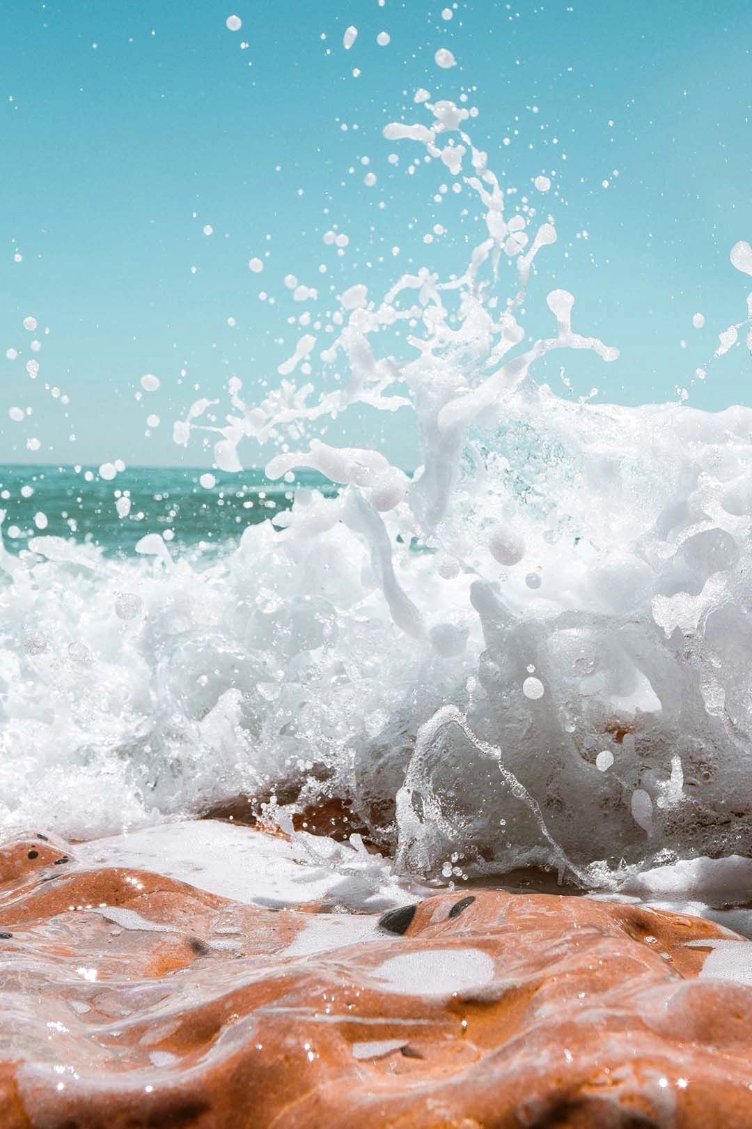 Ocean waves crashing against red rocks creating dramatic white water splash against turquoise sky.