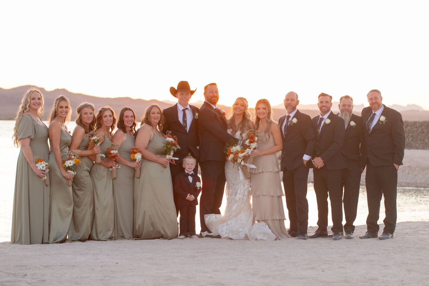 Bridal party in sage green dresses and dark suits at sunset on sandy beach, at The Riviera Marina in Lake Havasu Arizona.