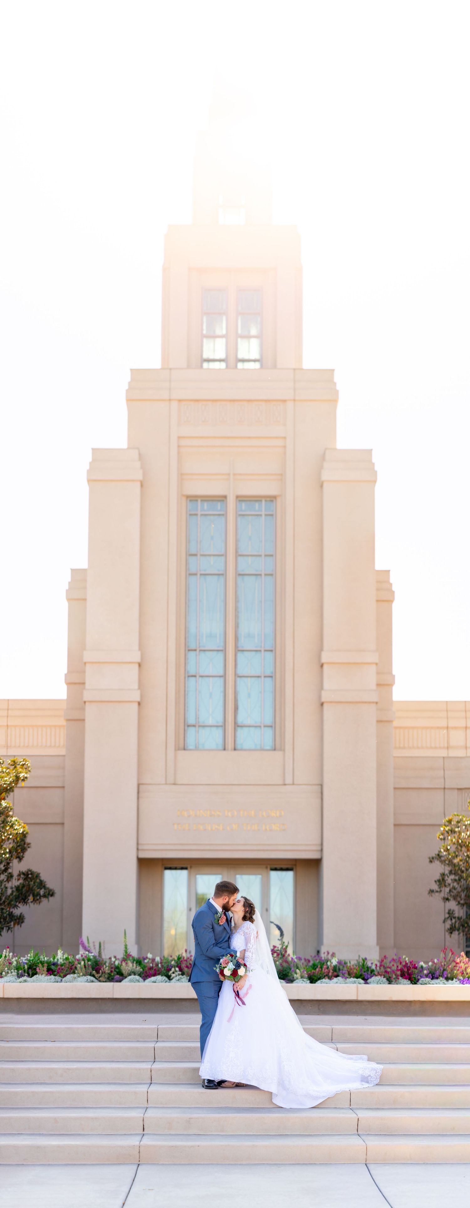 Bride and groom kissing on steps of an LDS temple on their wedding day, with a stunning Art Deco spire backdrop.