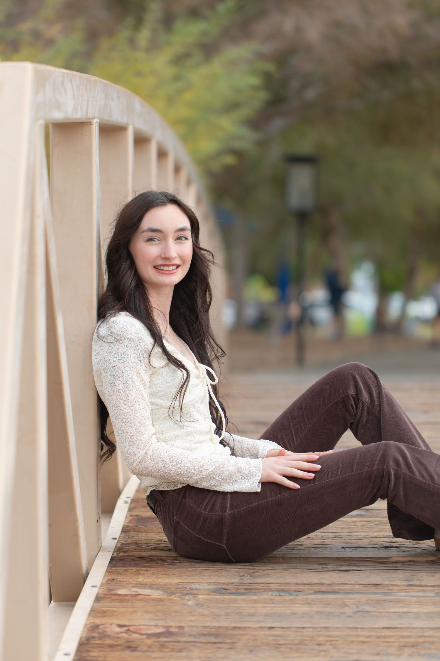 Young woman in lace top poses on wooden bridge railing at rotary park lake havasu during outdoor portrait session.