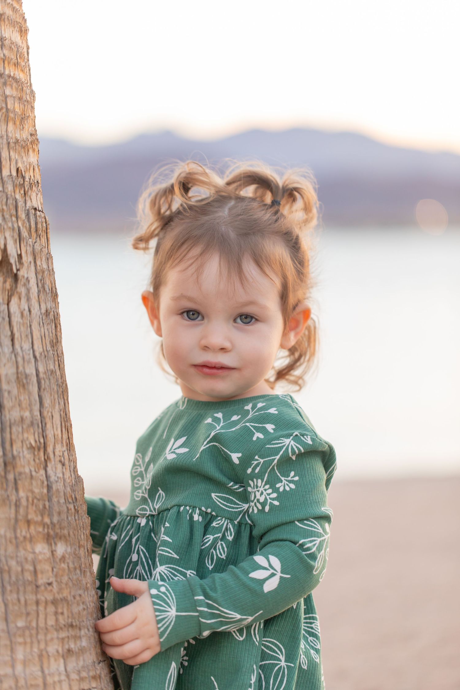 Small child wearing a green floral print jacket plays between wooden posts at the beach during sunset at Rotary park in Lake Havasu