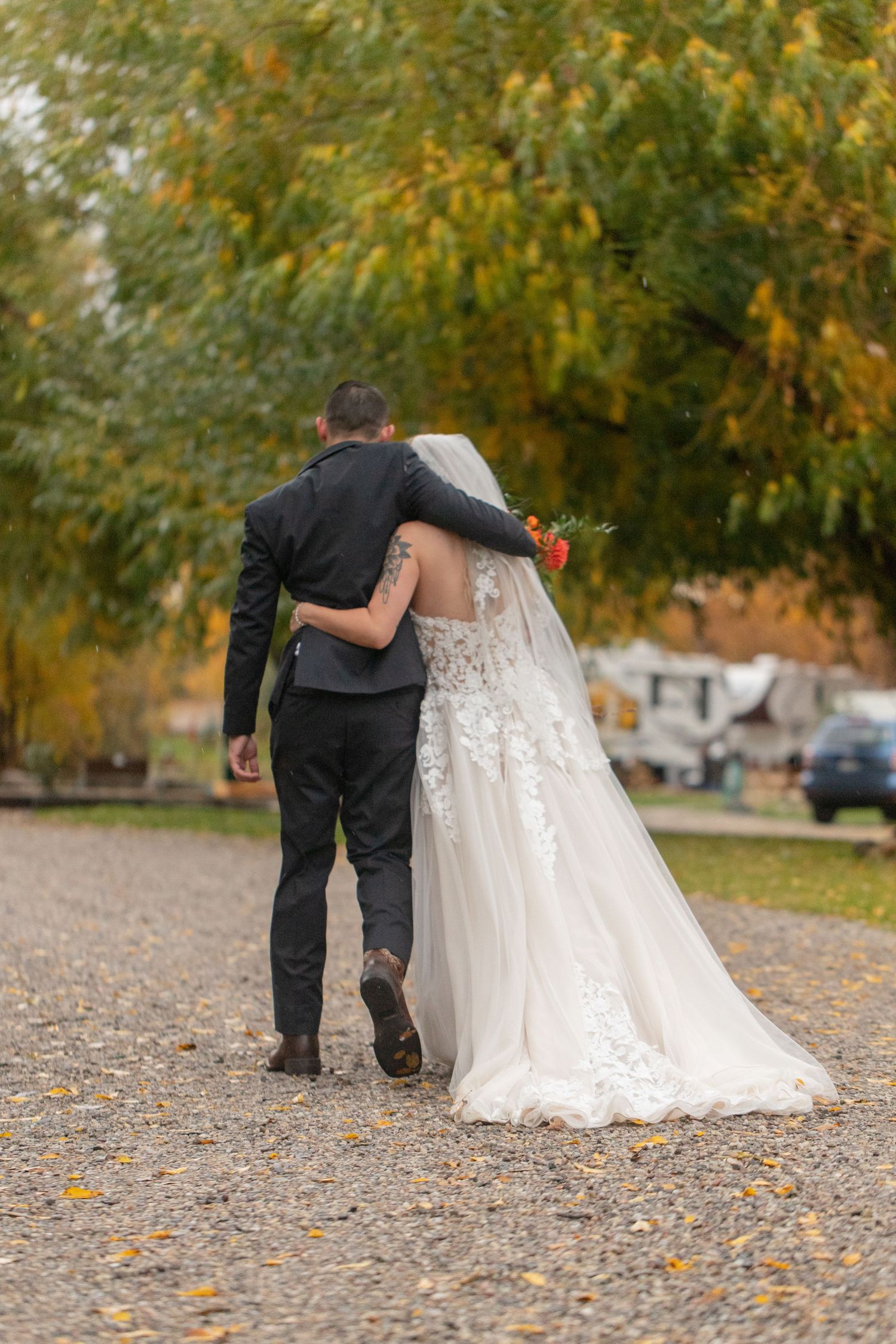 Couple walks together on gravel path with autumn trees creating golden backdrop.