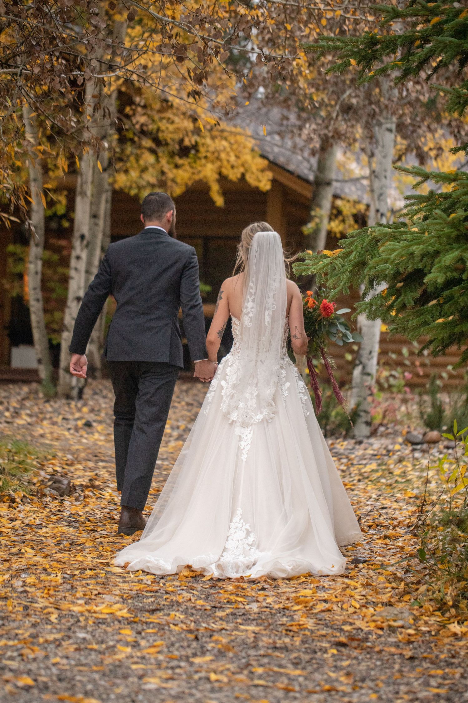 Wedding couple walks through path covered in golden autumn leaves.