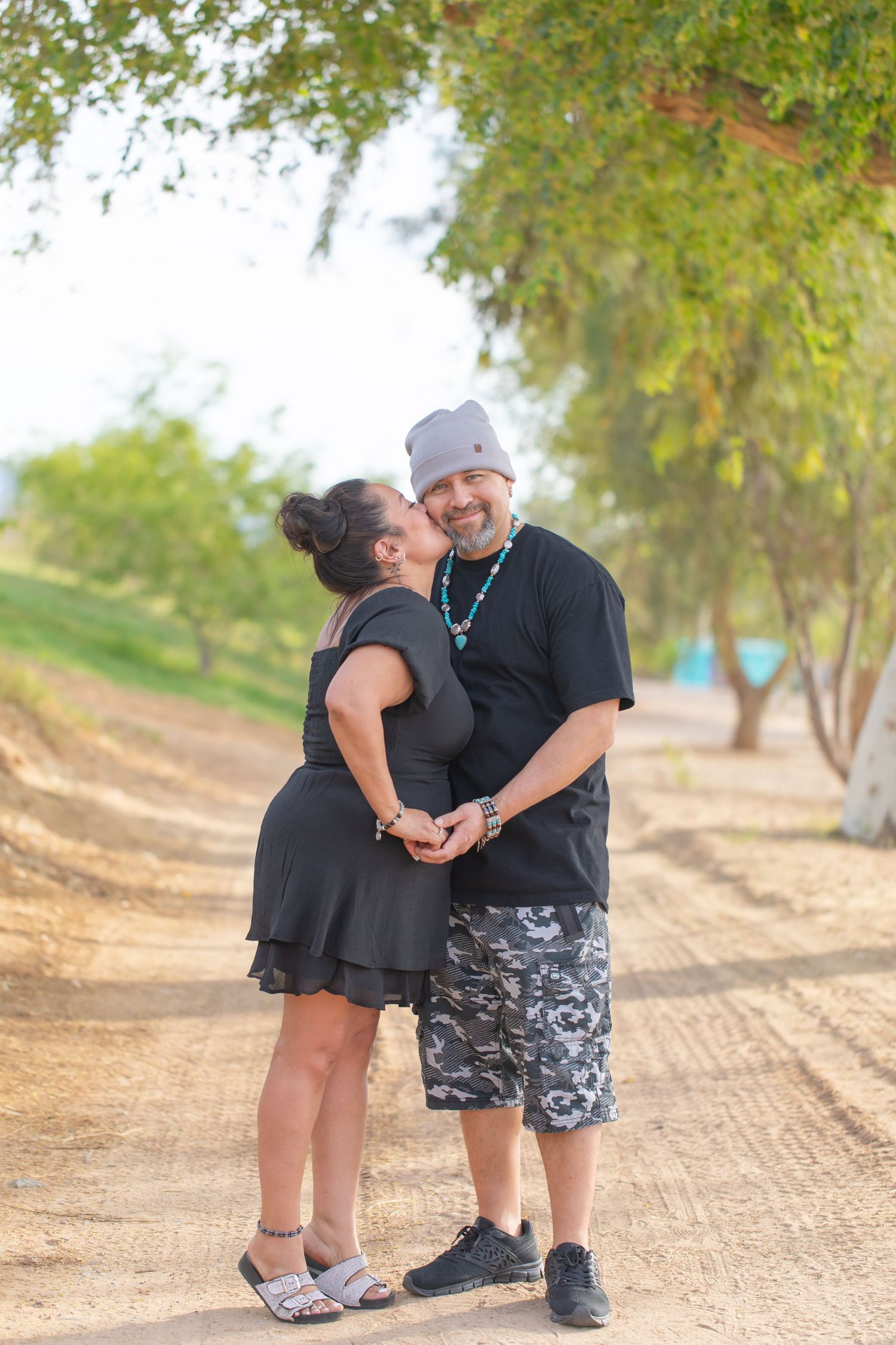 A couple shares a tender moment on a dirt path surrounded by green trees in a romantic outdoor setting.