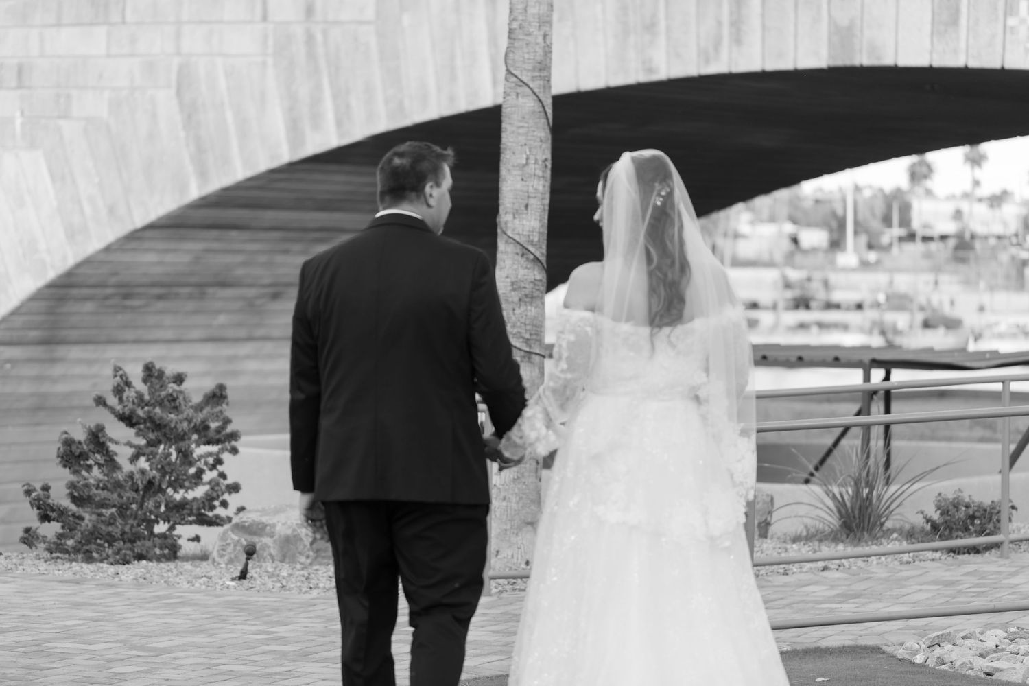 Bride and groom holding hands walking away under arch in black and white wedding photo at Shugrues in Lake Havasu City near the london bridg