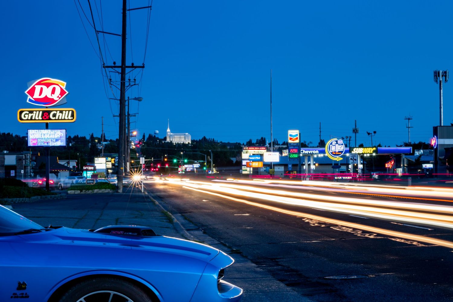 Night scene in Rexburg, Idaho with light trails from cars and illuminated signs along a dark highway.