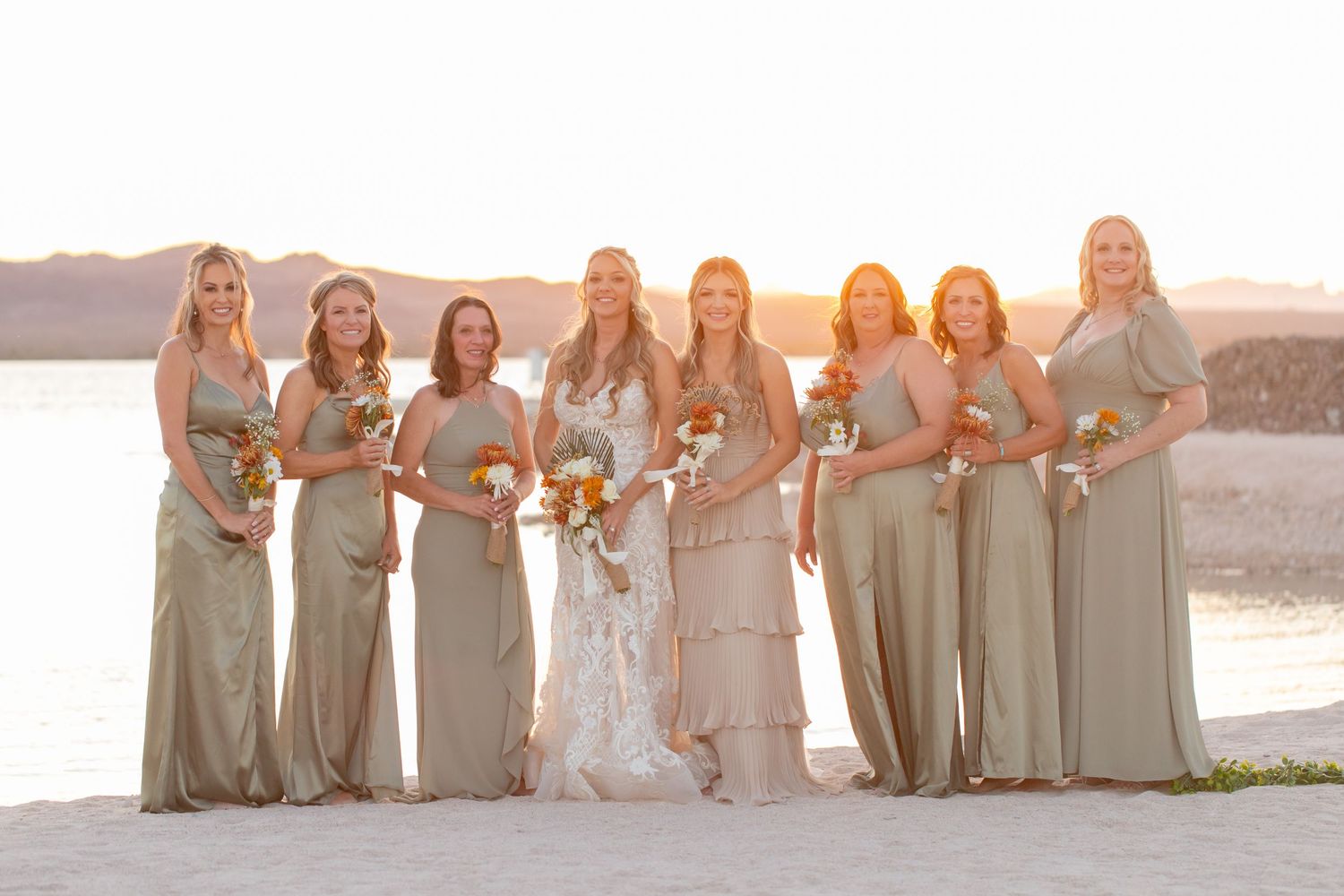 Wedding party in neutral dresses posed on beach at sunset.