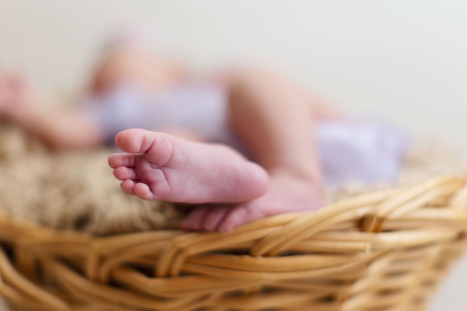 Close-up of tiny newborn baby feet resting in a cozy wicker basket with soft fur lining.