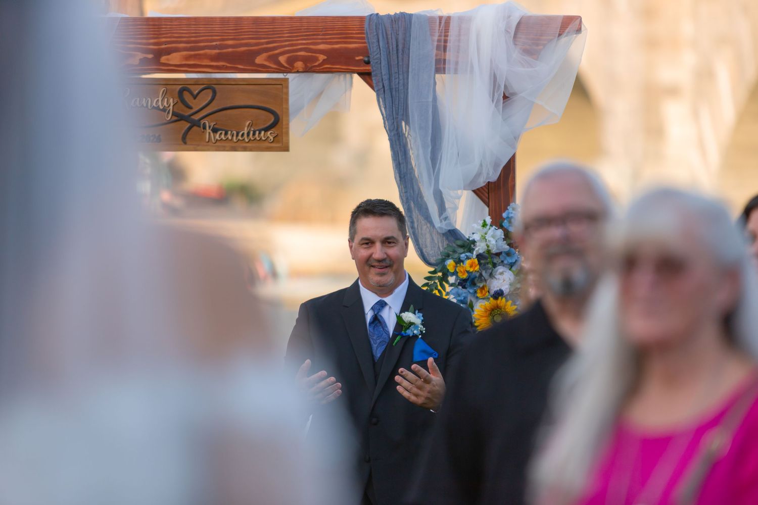 Groom smiling at bride during outdoor wedding ceremony with floral arch decoration at Shugrues in Lake Havasu