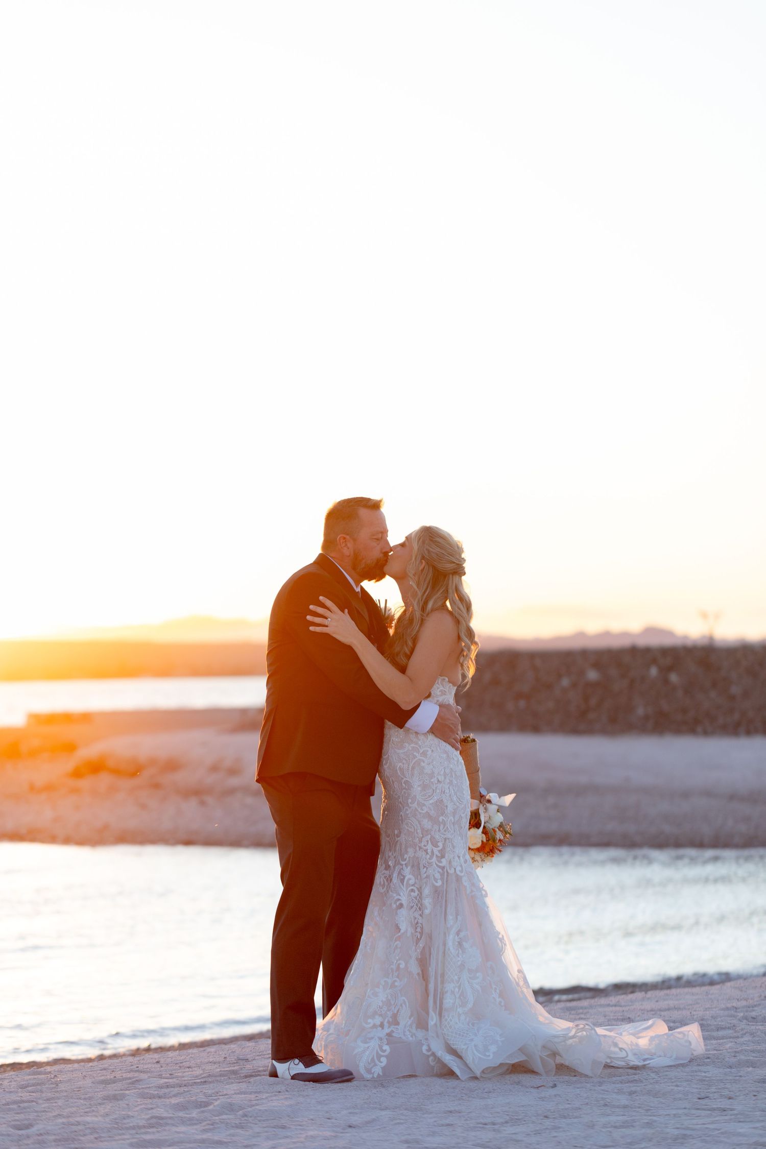 Wedding couple shares intimate moments on a beach at golden hour with ocean backdrop.