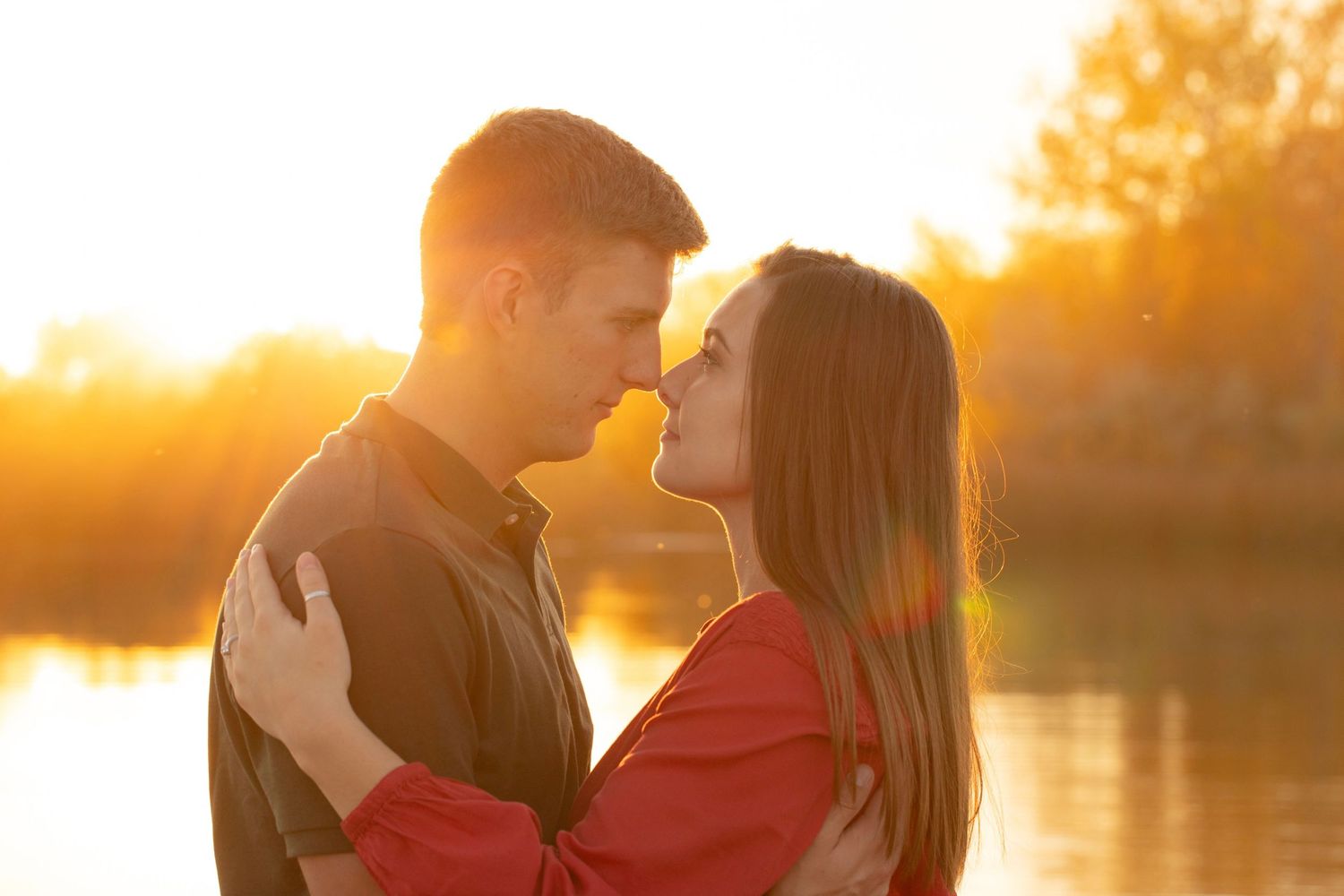 Romantic couple silhouetted against golden sunset by water.