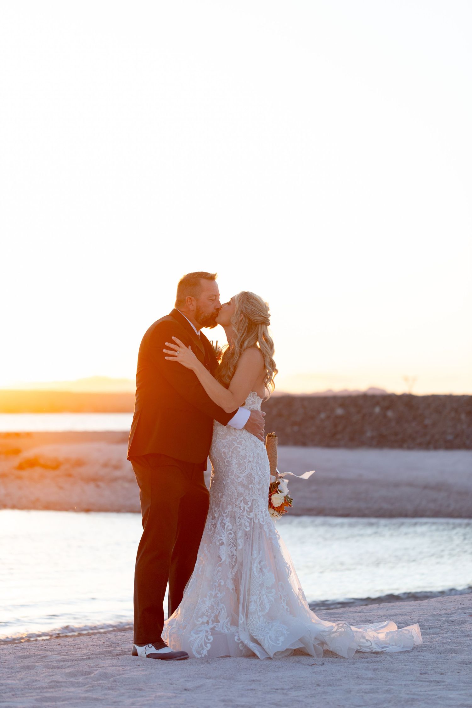 Romantic silhouettes embracing on a beach at sunset with soft golden light.