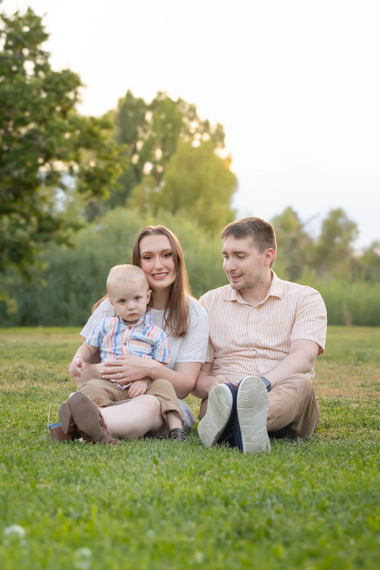 Family relaxing together on grass during summer evening photo session.
