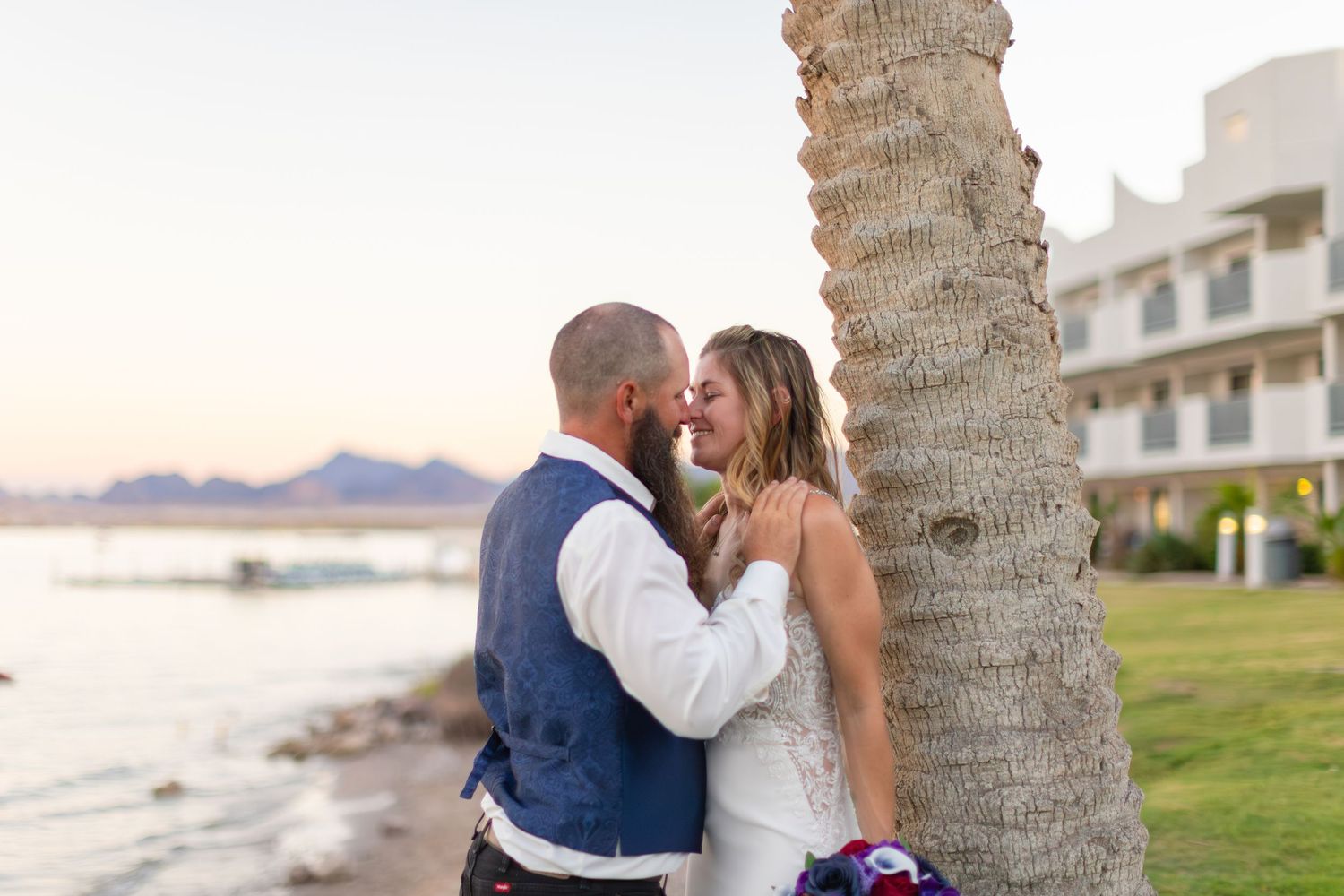 Newlyweds share romantic moments under palm trees at a beachside wedding at the nautical lake havasu during sunset.