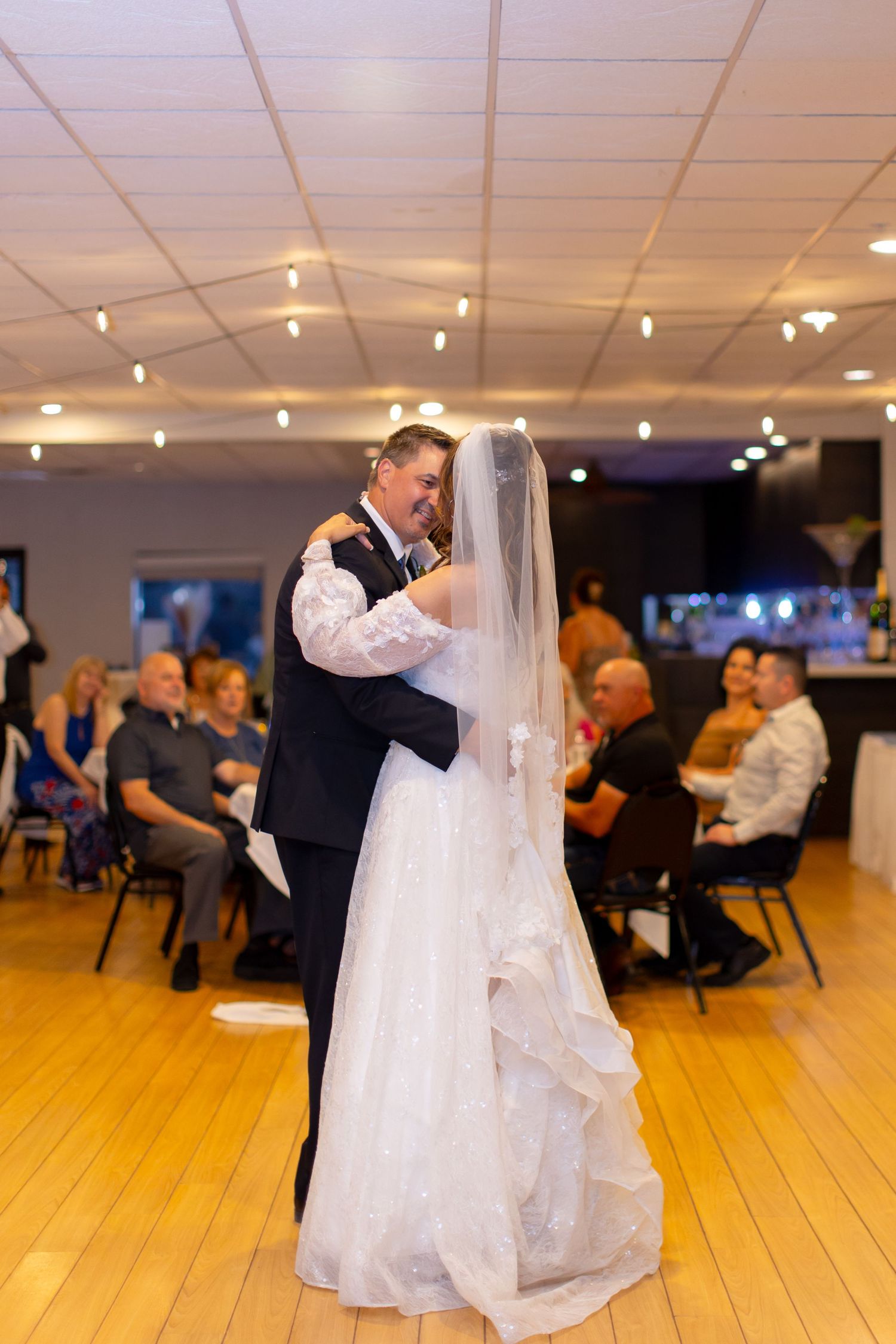 Bride and groom share their first dance at wedding reception, guests seated watching in warmly lit ballroom at Shugrues in Lake Havasu City