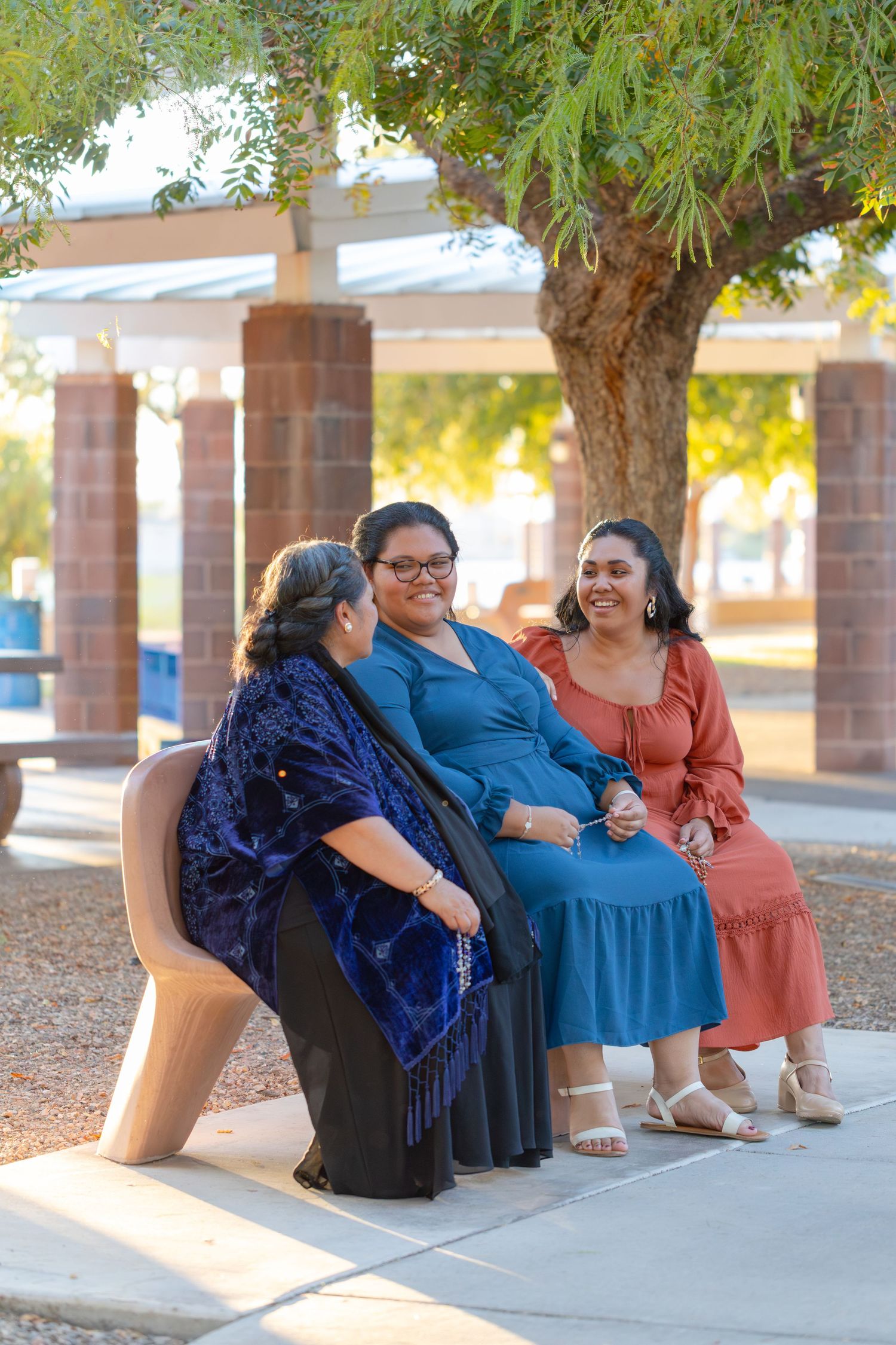 Family of three sharing a joyful moment while sitting outdoors under green trees at rotary park lake havasu.