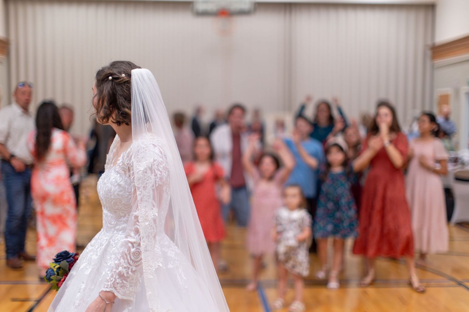 Wedding reception in a gymnasium with guests dancing and celebrating.
