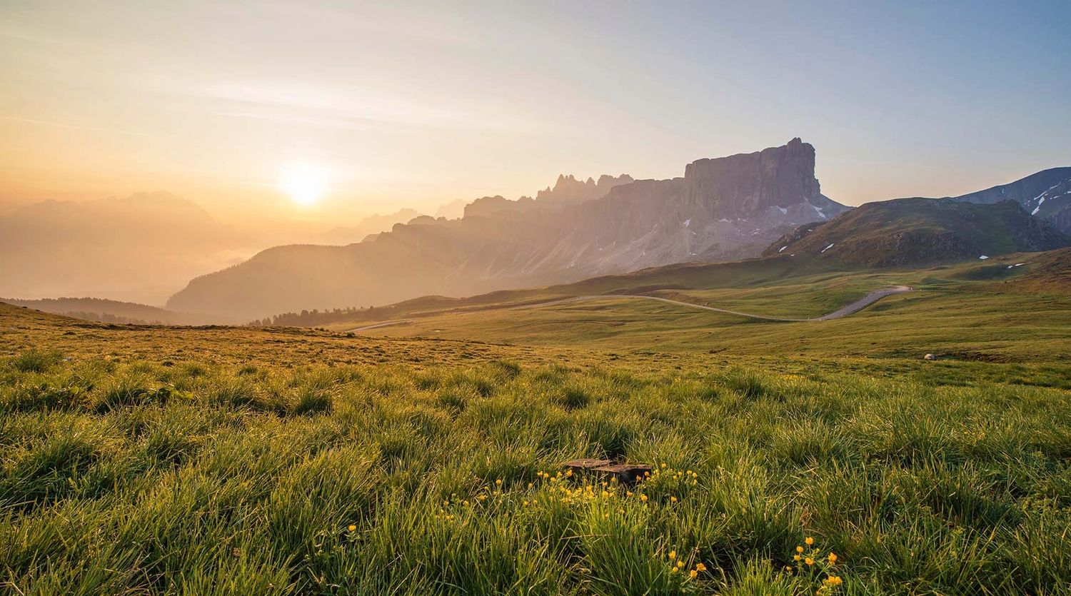 Scenic mountain landscape at sunset with lush green meadow in the foreground.