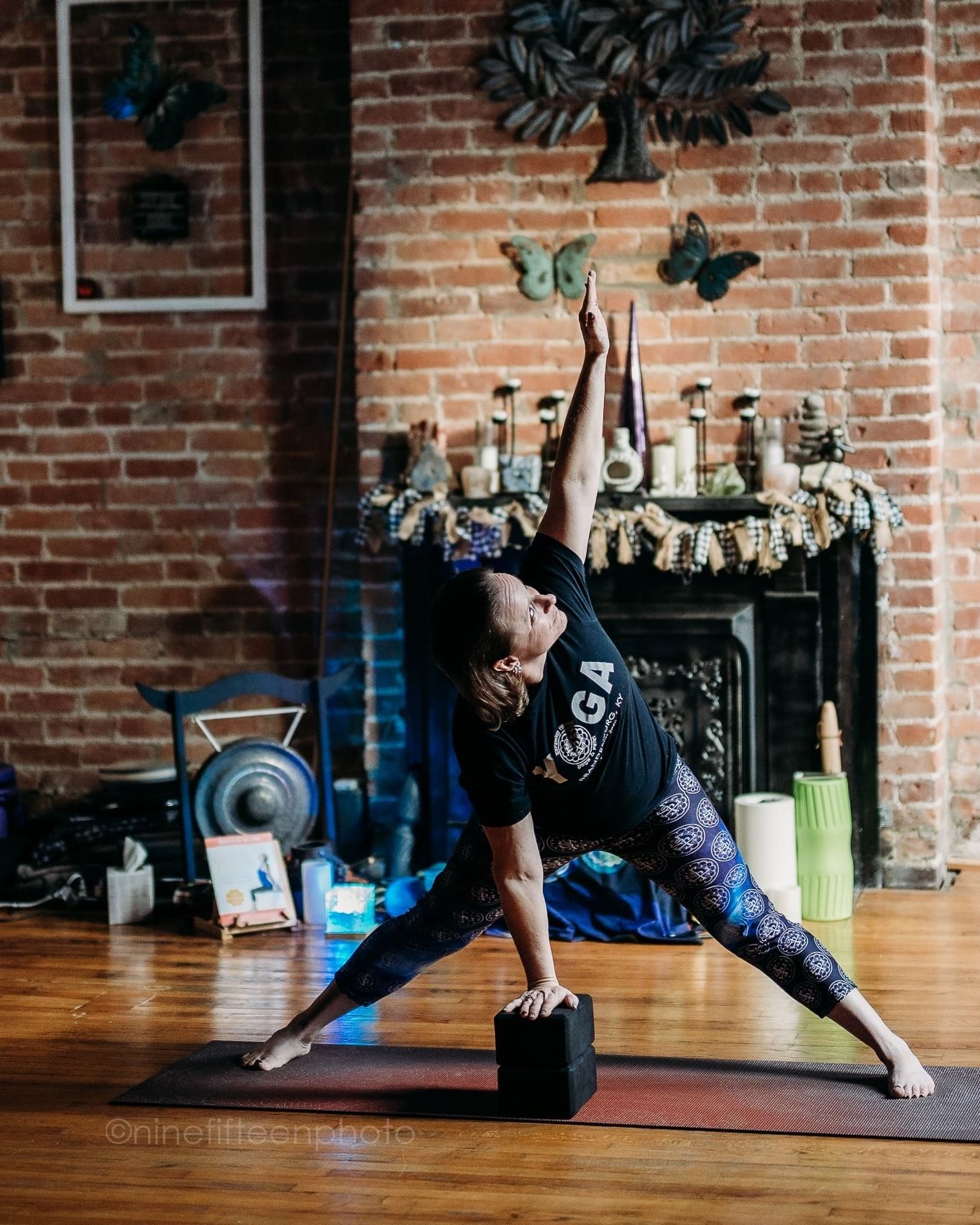 Yoga instructor performing extended triangle pose on mat in rustic brick fireplace studio.