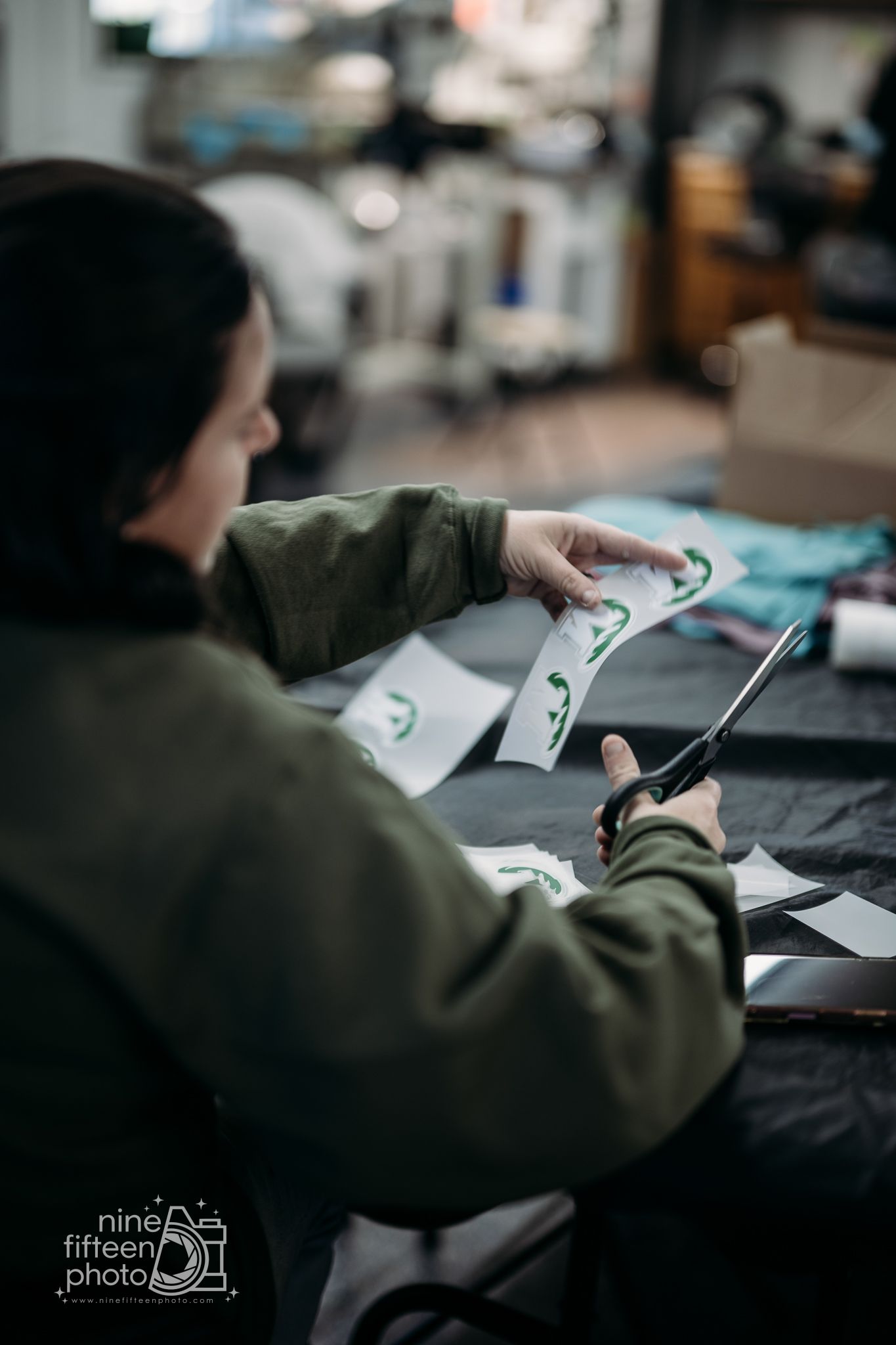 Worker in green jacket carefully cutting printed design sheets with scissors in a print shop.