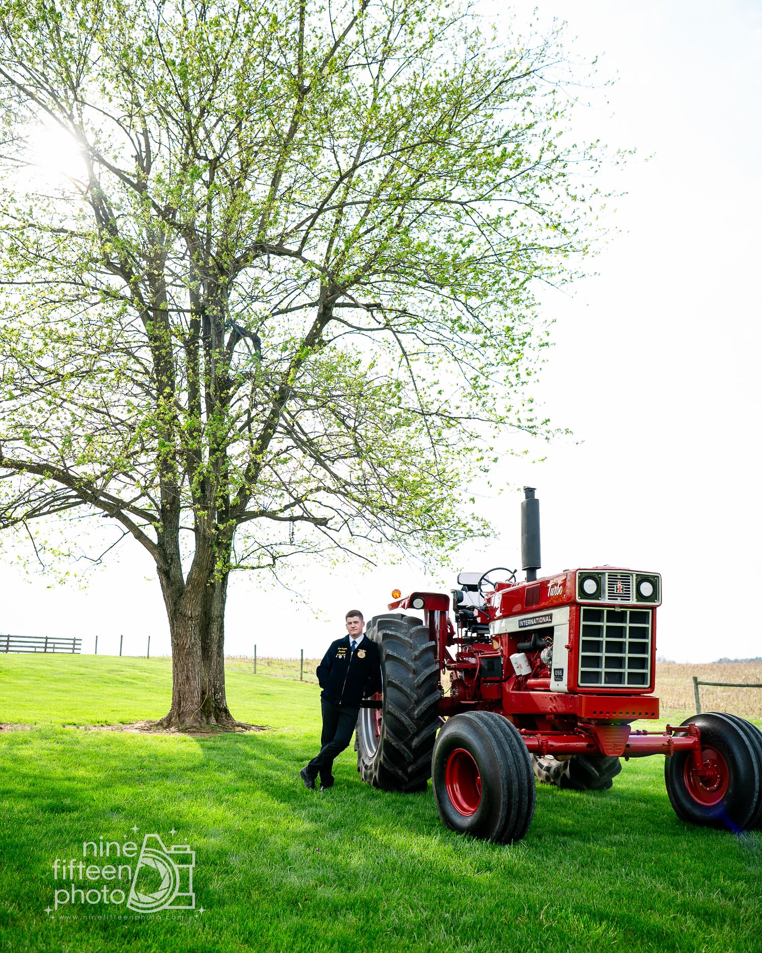 Person standing beside a classic red International Harvester tractor on a green farm lawn under a budding tree.