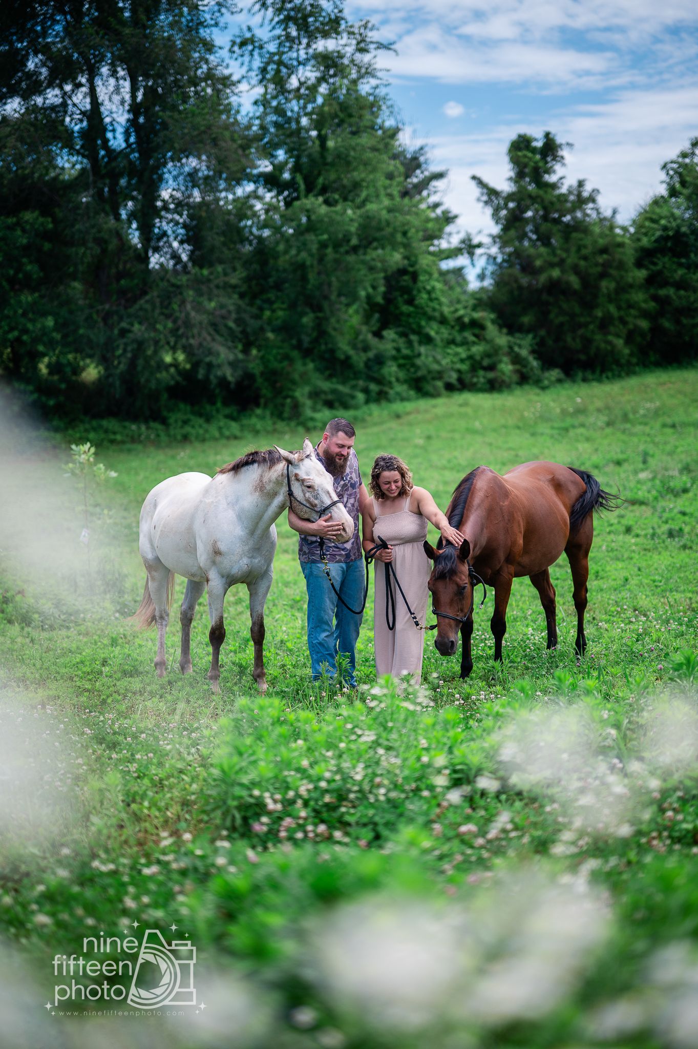 Couple standing in a lush green field with a white and brown horse, captured by Nine Fifteen Photo.