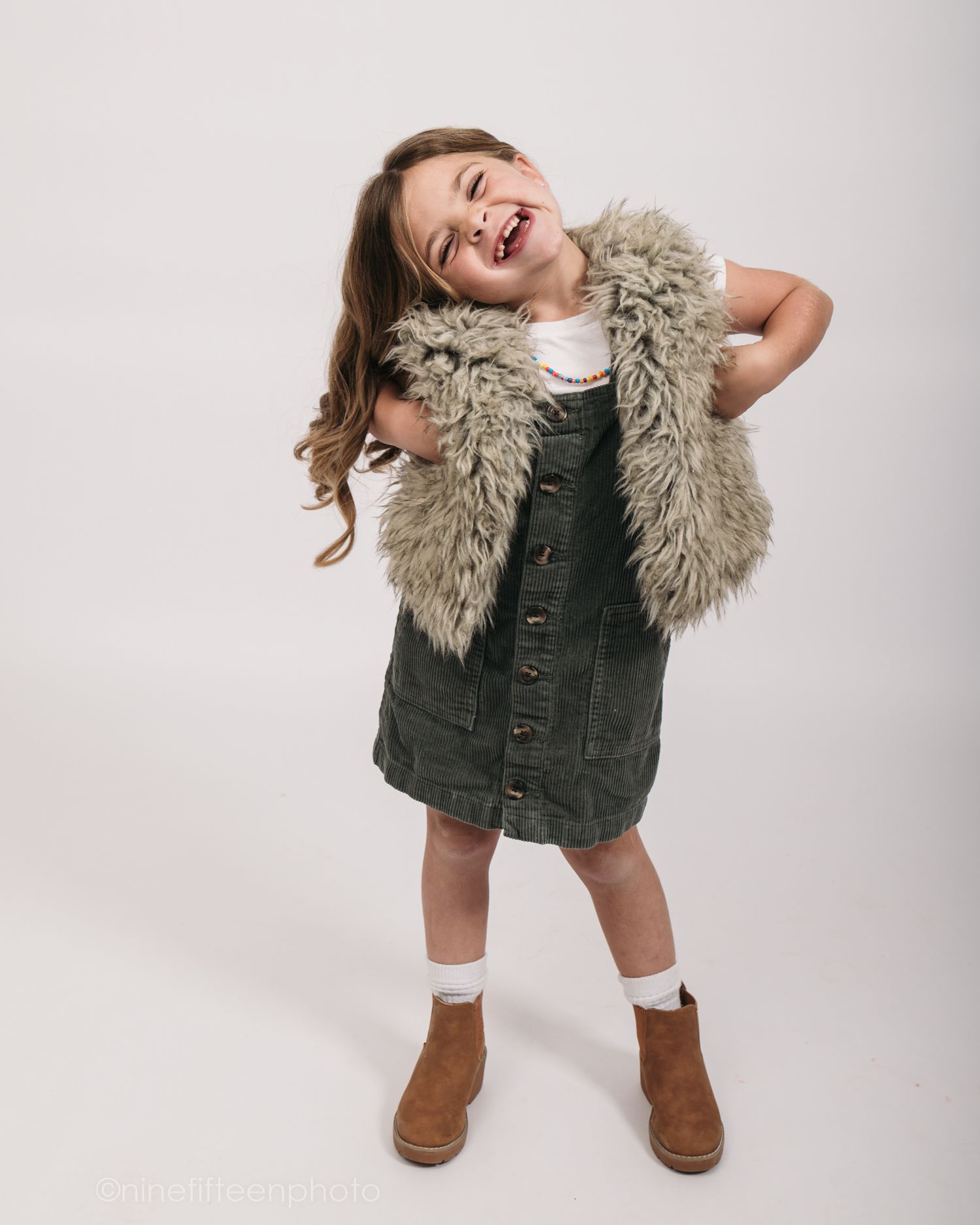 Studio personality portrait of a young girl smiling confidently in a textured vest against a neutral studio backdrop in Meade County KY