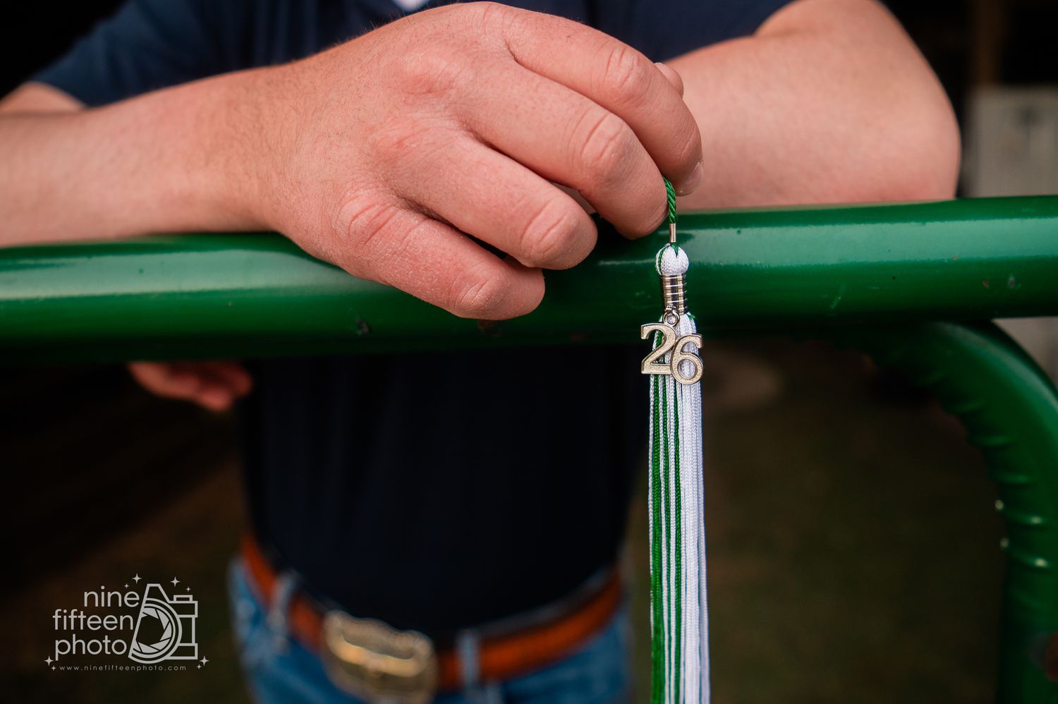 Man holding a green metal railing with a graduation tassel charm featuring the number 25.