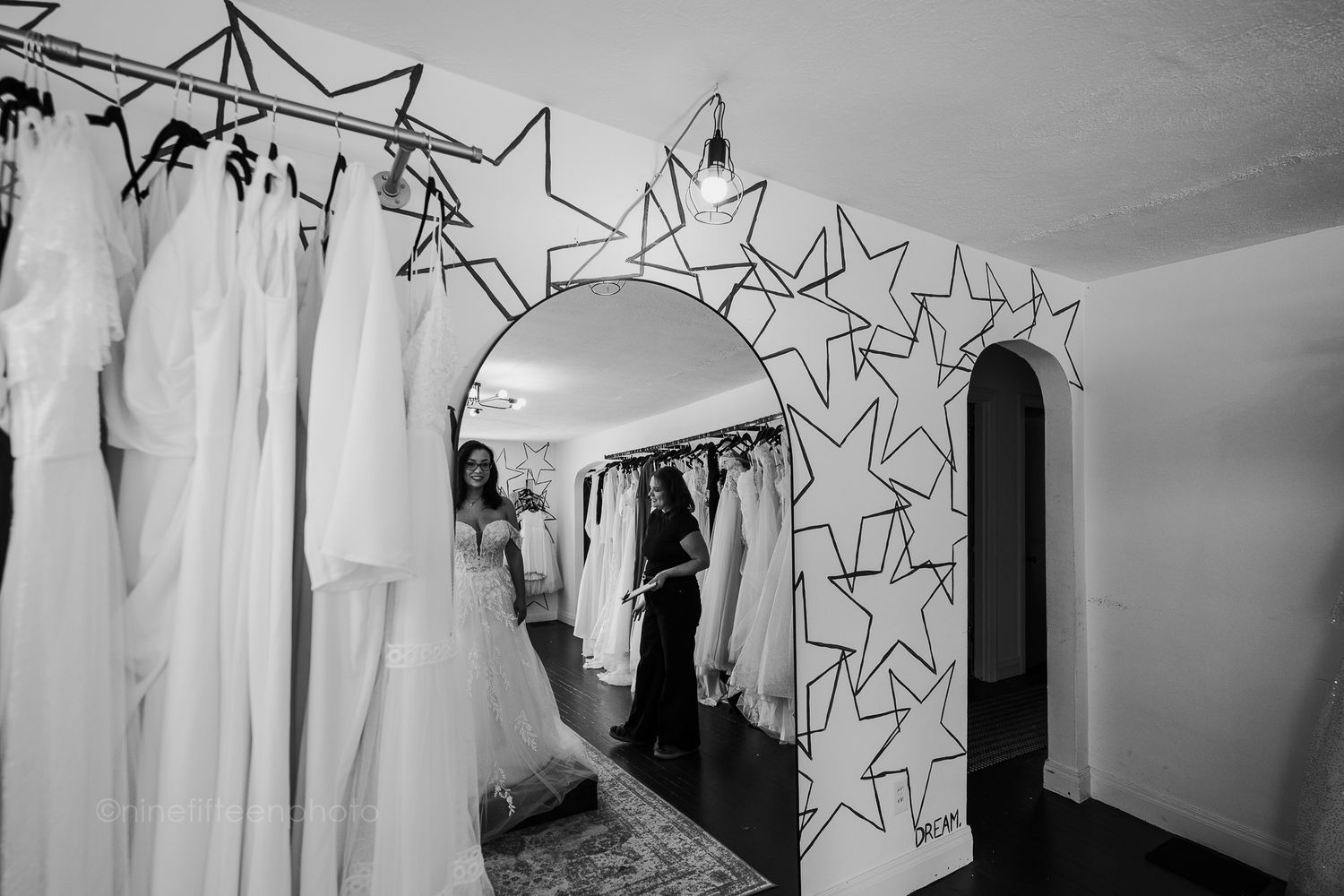 Black and white image of bridal shop mirror archway with star decorations and gowns.