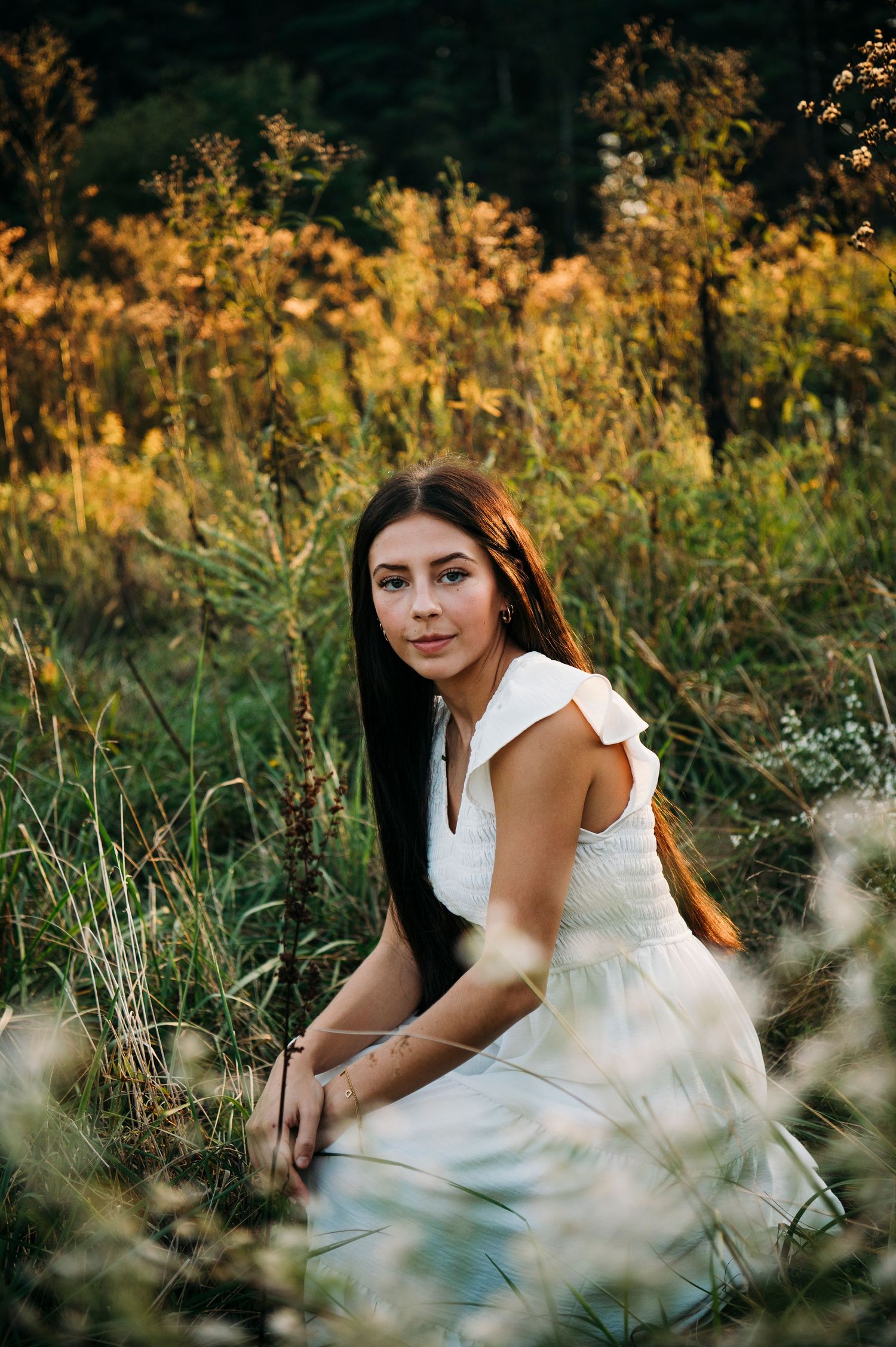 Emily sitting in tall grass surrounded by golden fall light during her senior photos at Otter Creek Park Brandenburg KY.