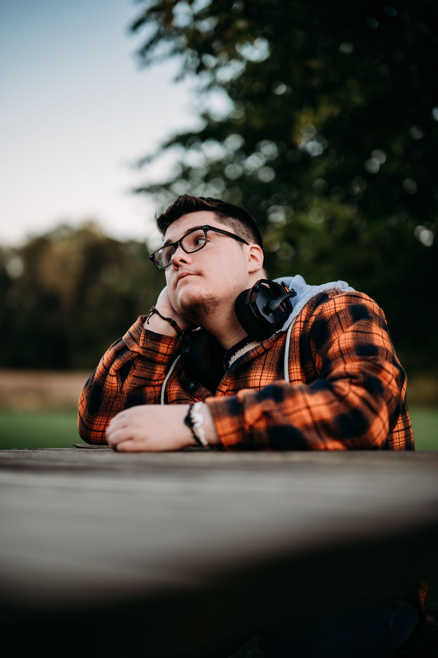 Luca sitting at a picnic table in his orange flannel during his Brandenburg KY senior session at sunset.