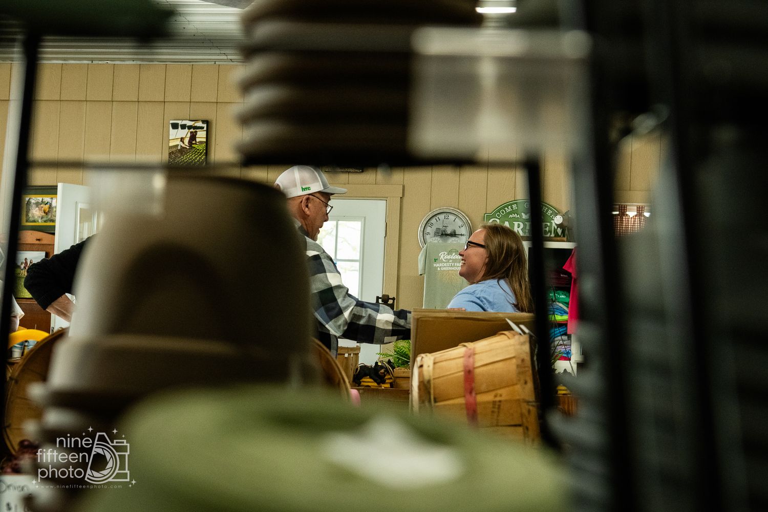 Two people conversing among wooden crates and merchandise inside a rustic farm market store.