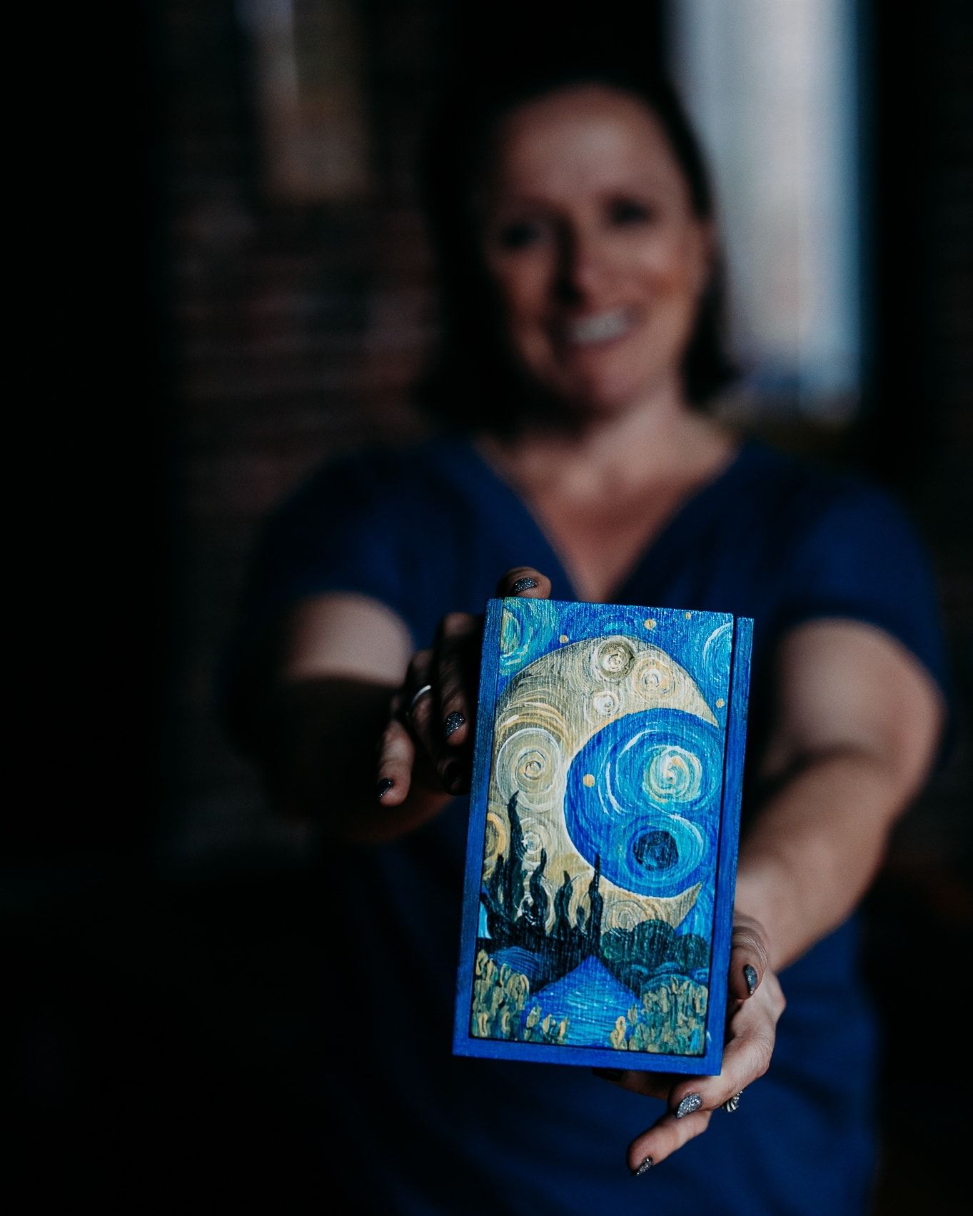 Smiling woman in blue top holds a Van Gogh-style painted tarot card box with swirling blue cosmic design.