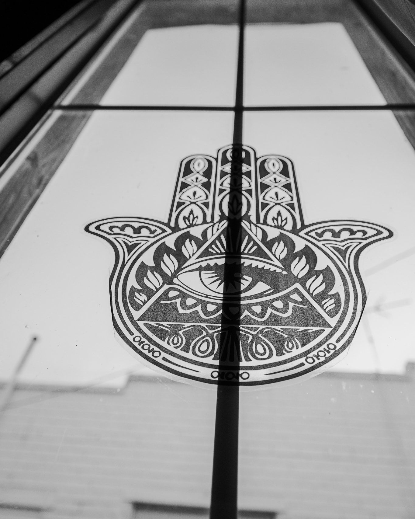 Black and white Hamsa hand symbol with evil eye printed on frosted window glass.