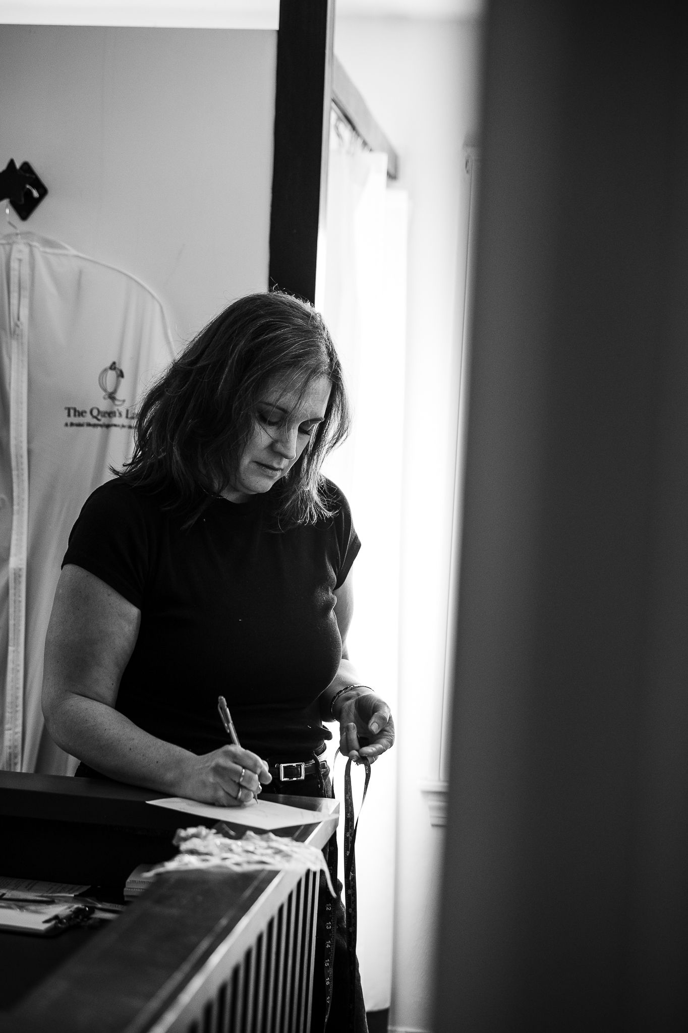 Woman in black top writing at a counter in a bridal boutique, black and white photo.
