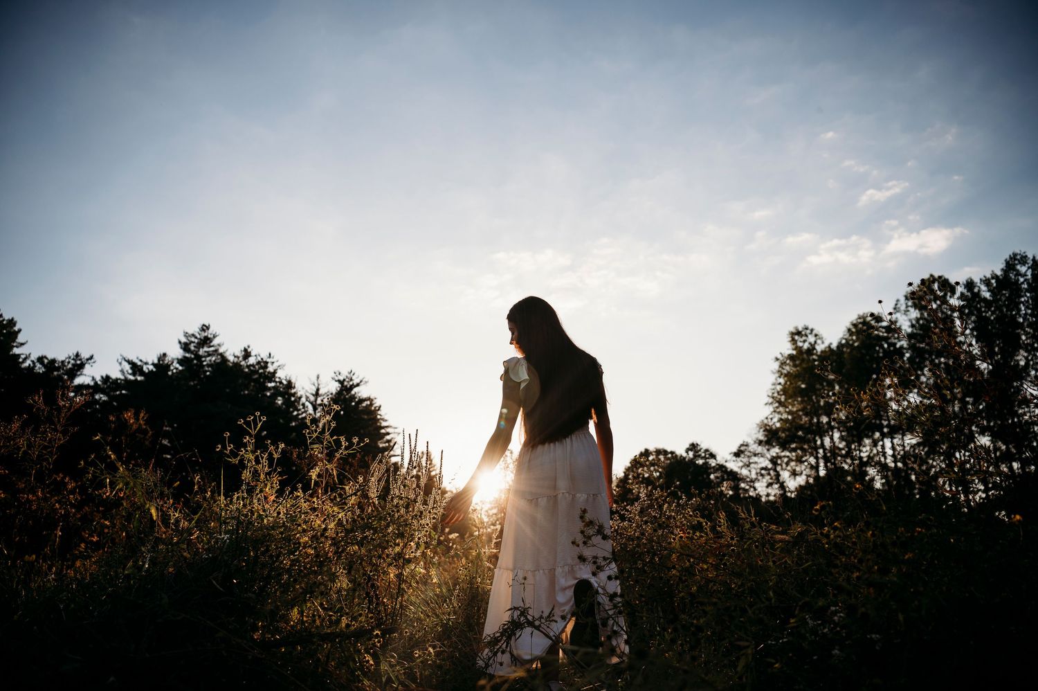 Emily walking through a sunlit field at sunset during her senior session in Brandenburg Kentucky.