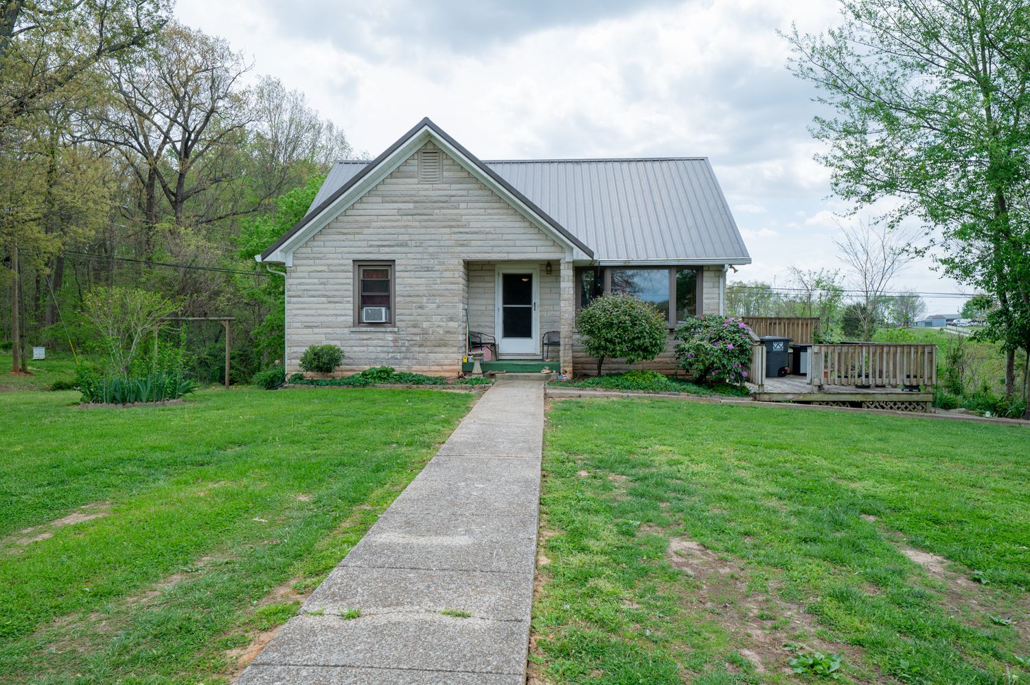 Charming white brick cottage with metal roof, covered porch, and lush green lawn in spring.