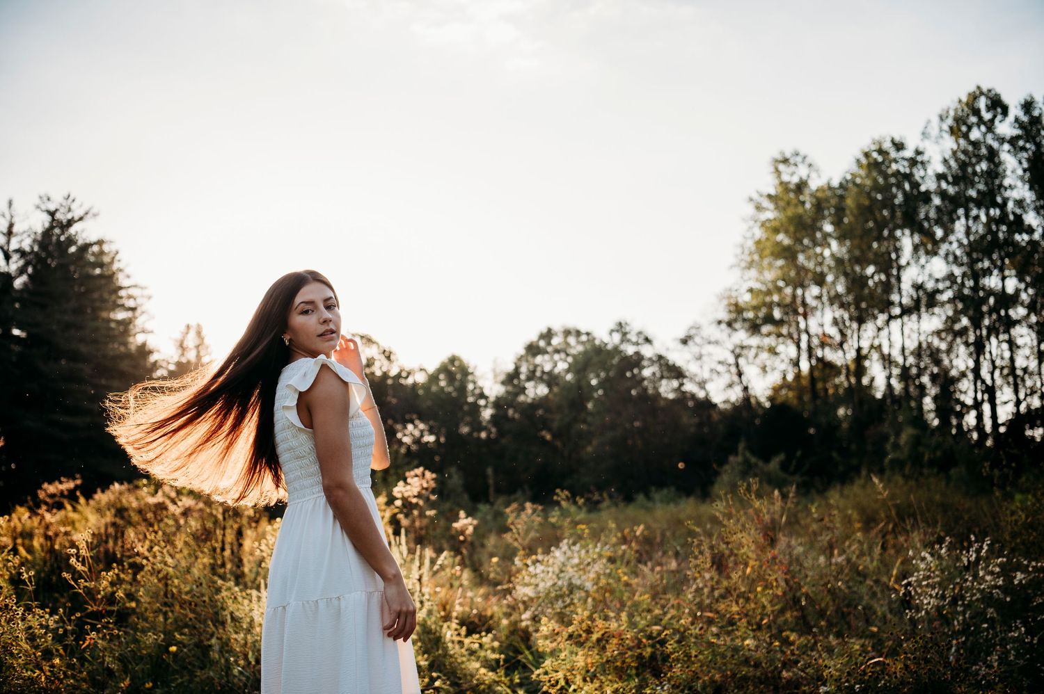 Emily walking through a sunlit field in her white dress during senior portraits at Otter Creek Park in Brandenburg KY.